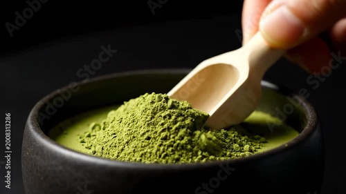 A close-up shot of a bowl filled with green powder, with a wooden scoop, against a dark background, showcasing the vibrant color and texture