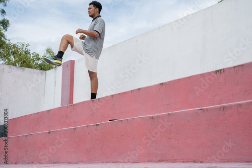 Man stretches before workout on stadium bench and stairs. grey shirt, white shorts, black socks.