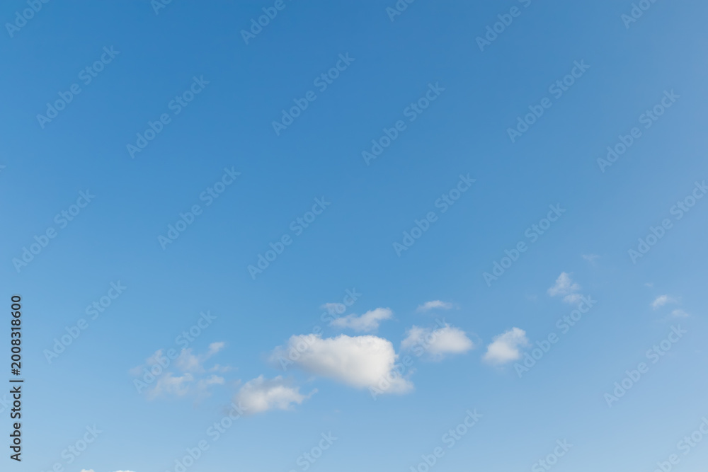 Fototapeta premium Minimalist view of a few small white clouds in the lower third of a vast clear blue sky