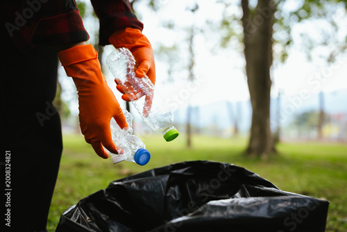 Tableau sur toile Person wearing gloves placing a plastic bottle into a trash bag in a park, highlighting recycling, environmental cleanup, and responsible waste management outdoors
