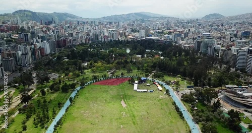 qAerial view of La Carolina Park central field in Quito Ecuador with city skyline and people in distance