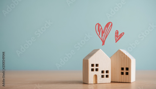 Two small wooden house models with hand drawn red hearts above them on a light blue background