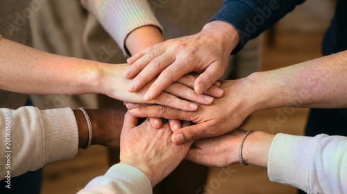 Group of diverse hands stacked together with soft rainbow light overlay