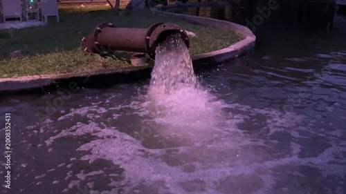 Water discharges from a large metal pipe into a canal, creating splashes and turbulence, industrial drainage system in outdoor setting, infrastructure managing flow, environmental and utility concept