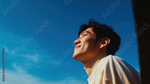 Young man looking up at a clear blue sky with a hopeful and serene expression, outdoor portrait