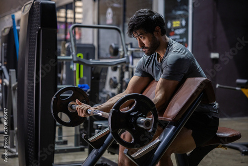 Barbell bicep curl gym fitness strength training Young athletic man doing barbell bicep curl preacher bench modern gym, focused expression, muscular arm workout with weight plate equipment