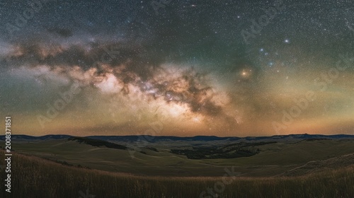 The Milky Way stretching across the sky above a serene valley, with rolling hills below 