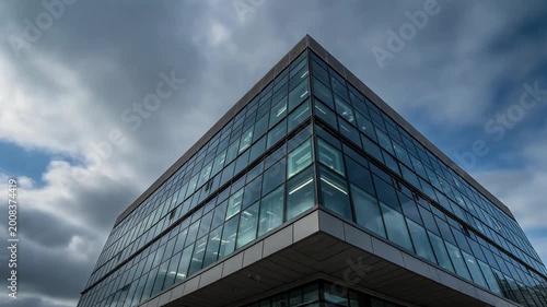 A large glass office building stands under a cloudy sky with blue patches.