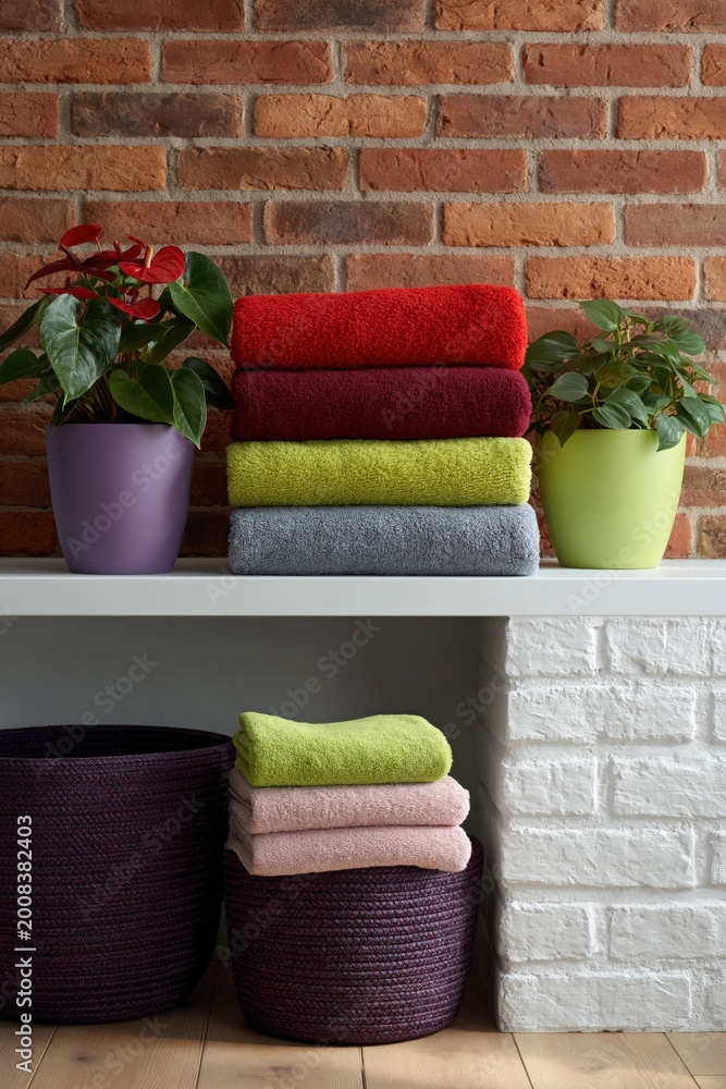 Fototapeta premium Stacked colorful towels with plants and baskets on shelves
