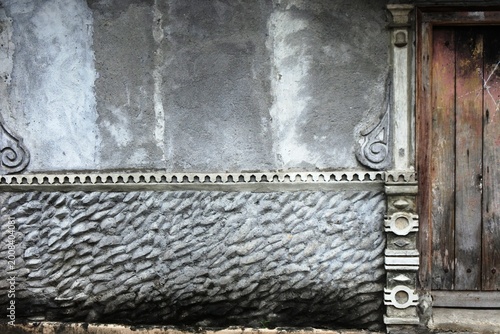 The house under renovation with rough textured plaster exterior walls and unique ornaments on the pillars with an old brown wooden door that has rotted on one side