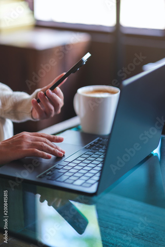 Vertical closeup image of a woman using smart phone and laptop computer