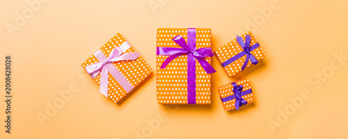 wrapped Christmas or other holiday handmade present in paper with purple and pink ribbon on orange background. Present box, decoration of gift on colored table, top view