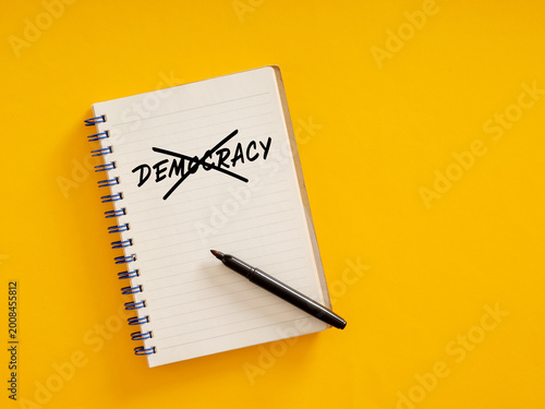 Notebook with crossed out democracy writing on yellow background