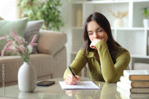 Pensive young woman filling out form on a coffee table