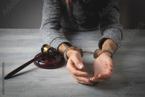 Man in handcuffs with a judge gavel on the table.