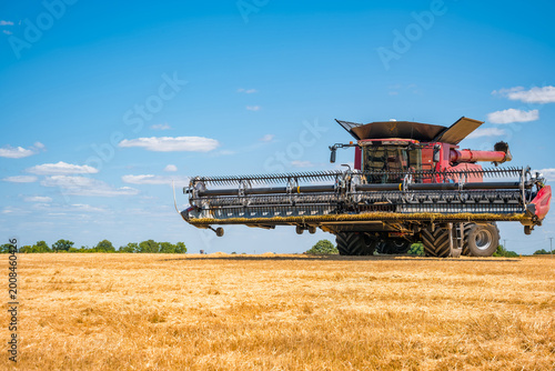 Tableau sur toile A red combine harvester operates in a golden grain field under a clear blue sky