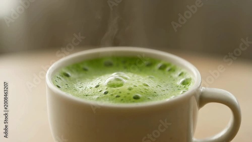 Steaming Hot Matcha Latte in a White Mug on a Table.