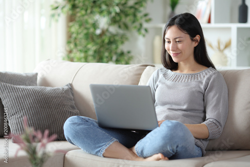 Satisfied asian woman using personal computer sitting at home