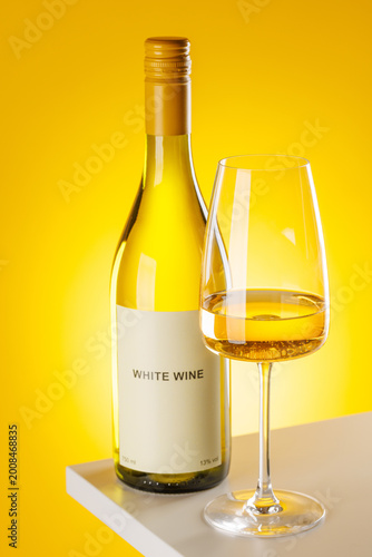 White wine bottle and glass on yellow background elegant drink setup