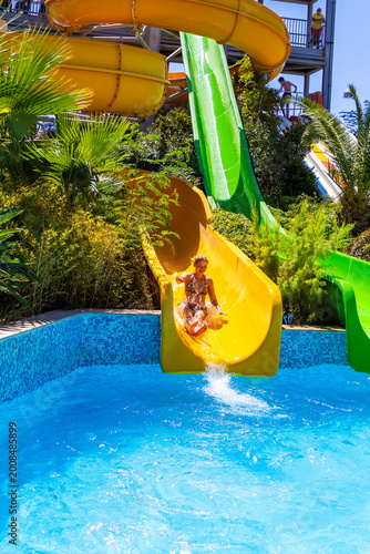 Obraz na plátně Young woman sliding down bright yellow water slide into pool with splash