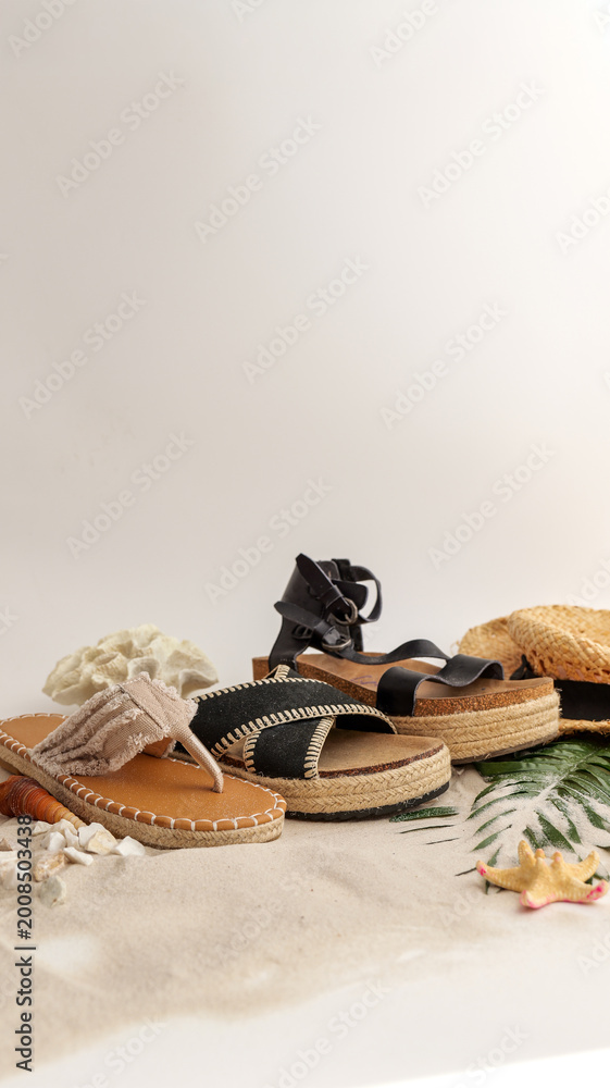 Naklejka premium Stylish summer sandals and straw hat arranged on a sandy beach with seashells
