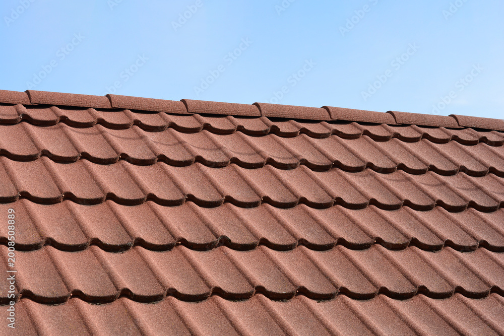 Naklejka premium An array of brown stone coated metal tiles covers a roof under a clear blue sky creating a textured repeating pattern