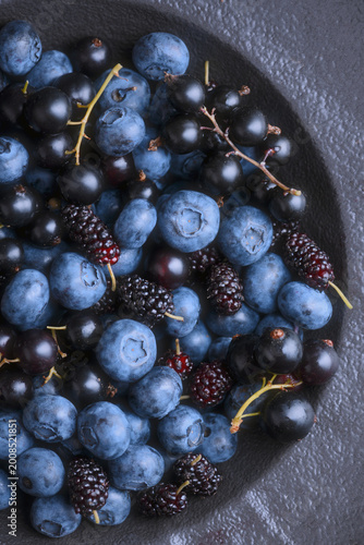 Close perspective of blueberries and mulberries in bowl, rich dark tones. Fresh summer berries, natural food styling