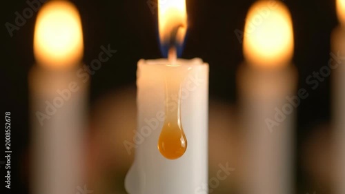 Close-up of a melting white candle flame dripping wax with other blurred candles in the background creating a warm soft glow and intimate atmosphere of light and shadow