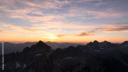 Majestic mountain range landscape featuring jagged peaks and layered horizons with a dramatic sunset sky displaying vibrant orange and purple clouds creating a serene and breathtaking atmosphere