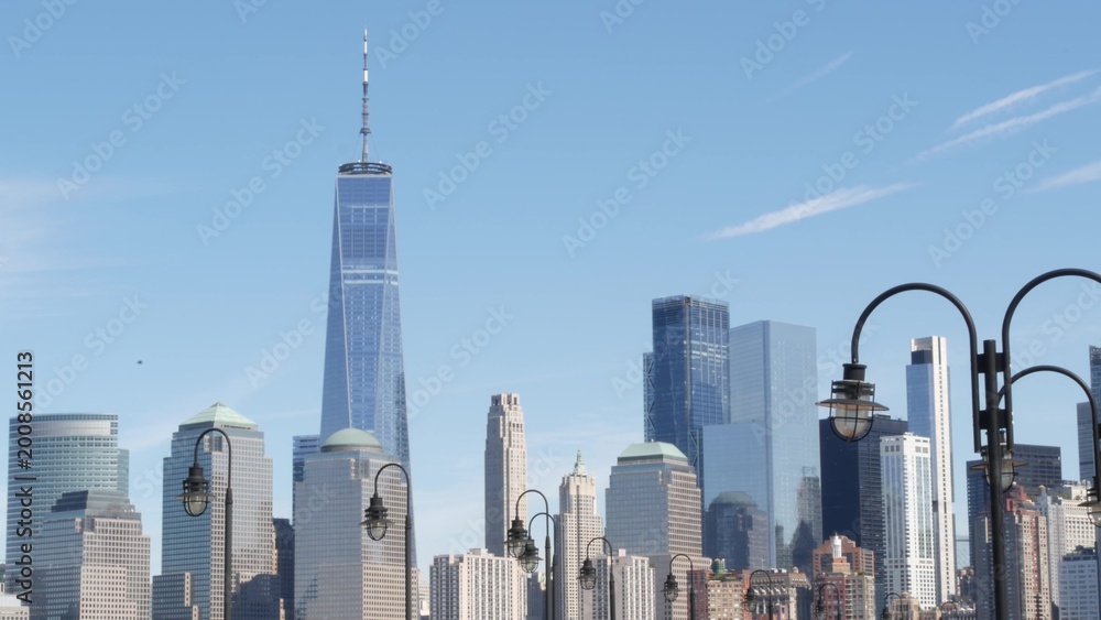 Fototapeta premium New York City Manhattan Downtown Financial District skyline, World Trade Center tower from New Jersey Liberty state park, United States. Pier lantern lamps and urban cityscape, skyscraper buildings.