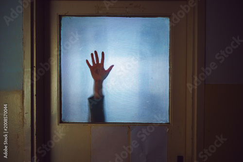 Hand of a woman sliding down stained glass door, eerie horror scene suggesting distress and confinement