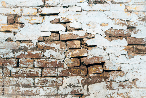 Texture of old damaged cracked weathered brick wall, thick layers of white paint are cracking, flaking and peeling of
