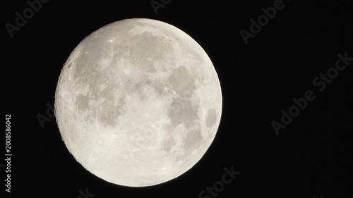 A detailed close up shot of a glowing full moon showcasing its craters and surface texture against the dark night sky background.