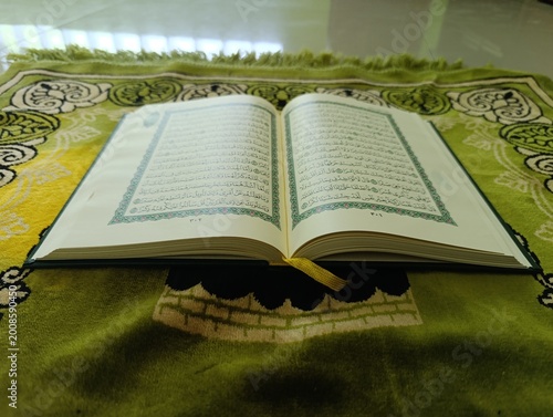 Open Holy Quran resting on a green prayer rug with traditional patterns inside a room