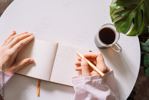 Woman writing in notebook near coffee cup on table.
