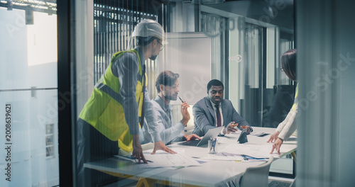 Executives and Engineers Meet in a Glass Conference Room to Review Construction Plans, Align Budget and Schedule, Track Progress on Laptops, and Coordinate Risk Control, Resource Allocation