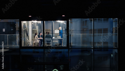 Night Office Meeting Shows a Female Manager Leading Three Coworkers Through a Clear Strategy Review, Using a Laptop, Charts, and Notes to Set Goals, Refine Plans, and Coordinate Upcoming Projects