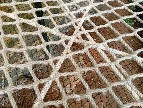 Close up of woven rope hammock net texture with geometric pattern above natural ground background outdoors. Detailed rope mesh hammock surface with rustic outdoor design and abstract woven texture