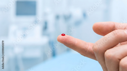 Close-up of a person's finger with a drop of blood on the tip, likely for a medical test or diagnostic procedure