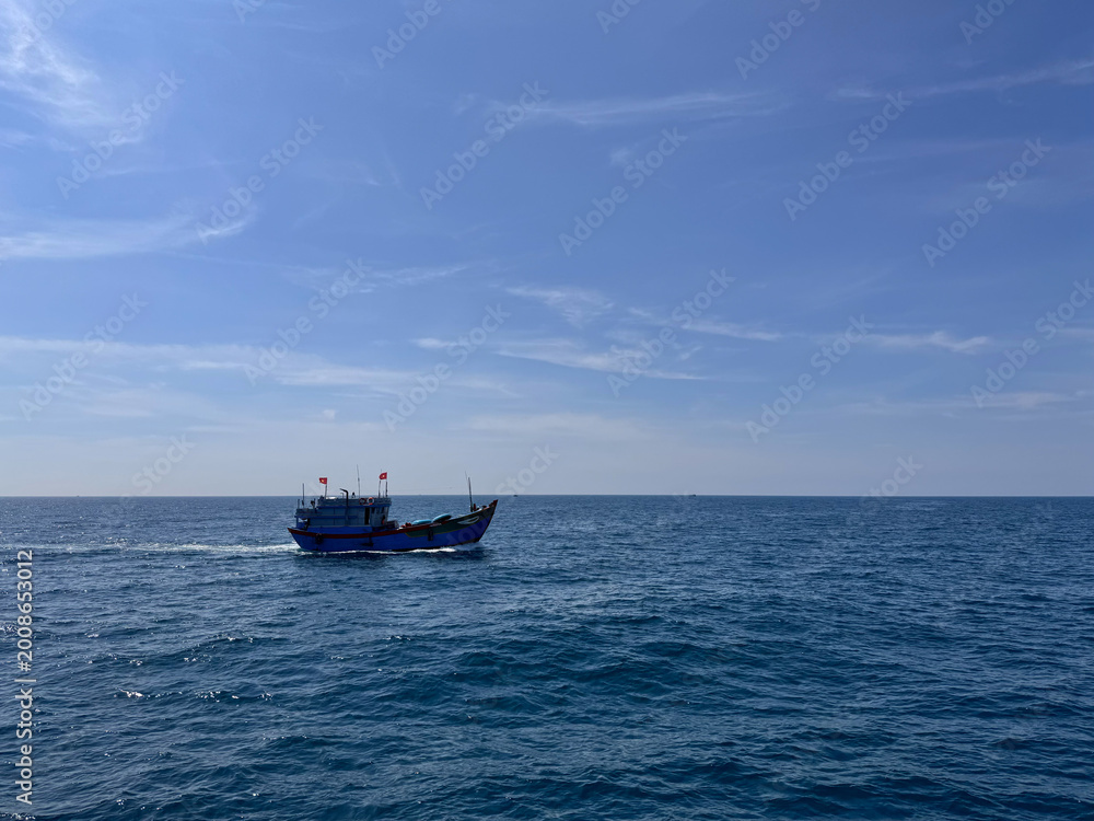 Obraz premium Lone fishing boat moving across the vast blue waters of the ocean