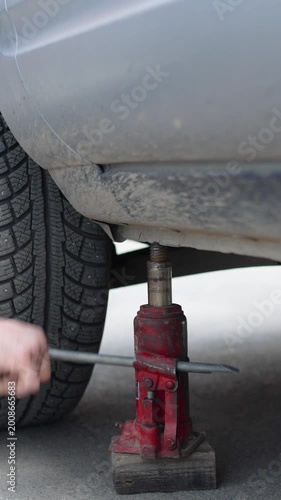 Experience the power of DIY car maintenance with a close-up of a man's hands expertly maneuvering a hydraulic jack. As he lifts the car, you can feel the anticipation of important wheel repairs ahead.