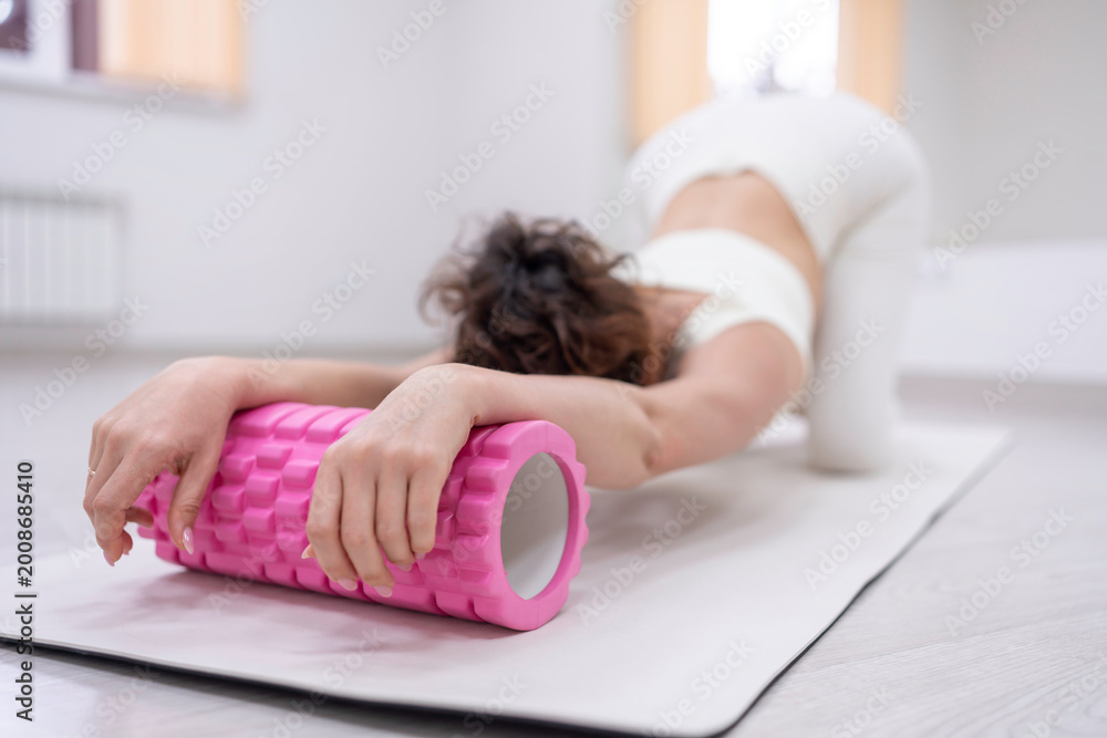 Fototapeta premium Foam roller stretching yoga woman performs myofascial release on mat in light studio for muscle recovery