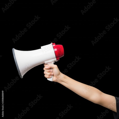 A human hand holding a white and red plastic megaphone, isolated against a solid black background, side view of a handheld loudspeaker