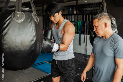 Canvas Print Young Asian man does boxing uppercut drill at the gym, guided by a trainer observing form and technique to improve timing, accuracy, and effective close-range combinations