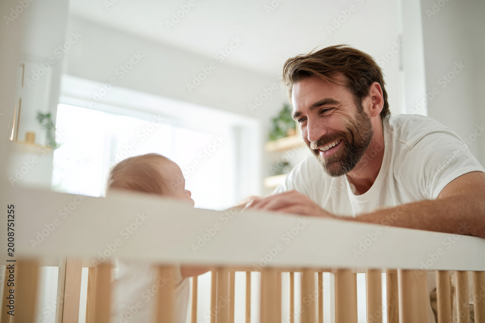 Fototapeta premium Professional scene of father smiling at baby while leaning on crib railing, medium close-up shot, bright modern nursery, natural daylight for marketing