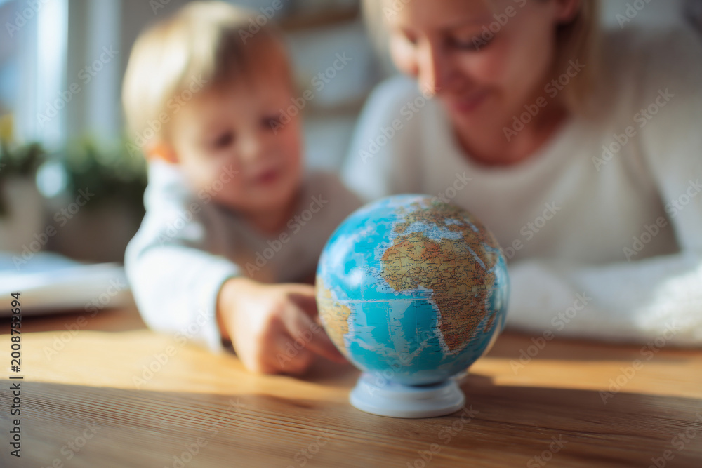 Fototapeta premium Mother and baby looking at globe placed on desk while planning imaginary travel, medium close-up composition, bright cozy home environment, natural daylight