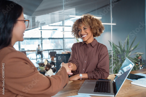 Fotografija Businesswomen shake hands at desk in modern business office, smiling at meeting