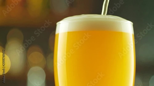 Golden beverage being poured into a frothy glass with bokeh background