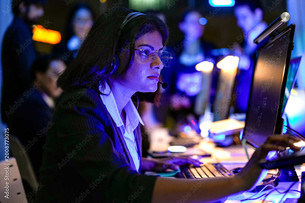 Obraz premium Professional female IT specialist working on a computer in a dark neon office at night. Focused expert analyzing network security and digital data in a modern high-tech command center.