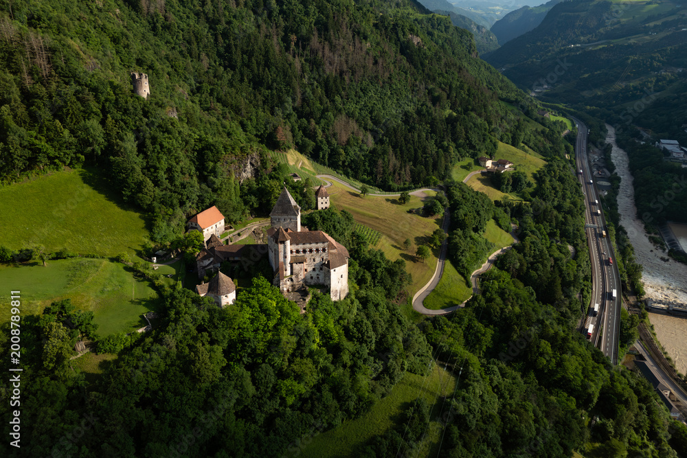 Fototapeta premium Trostburg Castle complex on a Dolomite slope, aerial view. Heritage landmark dominating the surrounding landscape